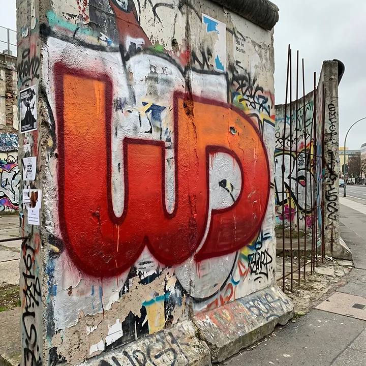 Graffiti-covered section of the Berlin Wall prominently featuring a spray-painted red Womp Designs logo.