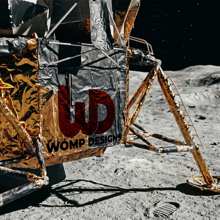 Apollo lunar module on the moon's surface bearing a red Womp Designs logo.