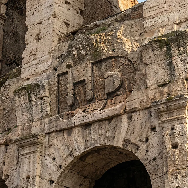 Ancient stone archway of the Roman Colosseum with a carved Womp Designs logo.