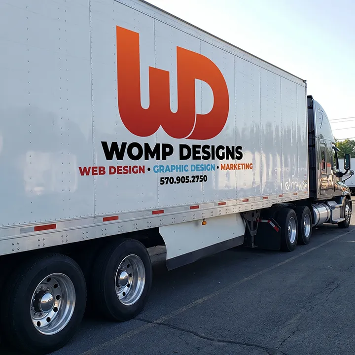 Commercial semi-truck trailer featuring orange and black Womp Designs advertising.