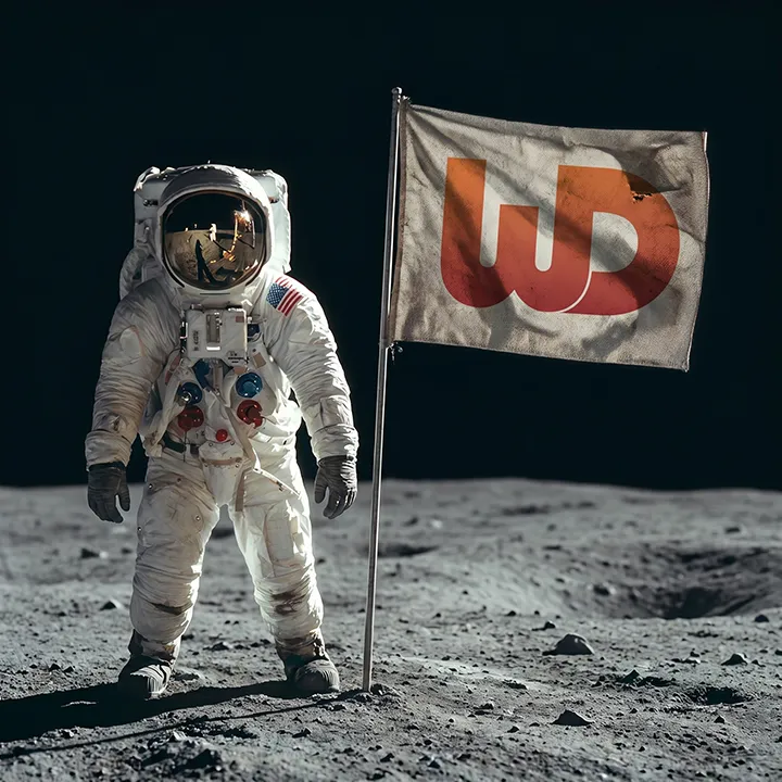 Astronaut standing on the moon's surface next to a planted flag featuring a large orange Womp Designs logo.